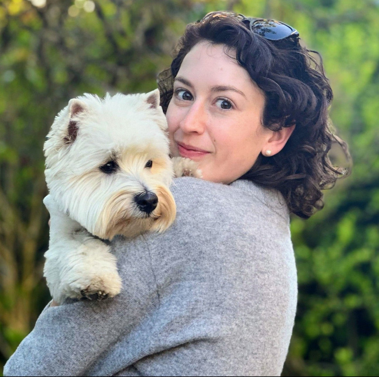 Woman holding a small white dog with a blurred green outdoor background