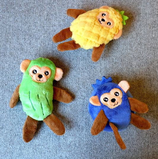 Three plush monkey-shaped accessories in yellow, green, and blue, arranged on a textured gray fabric background.